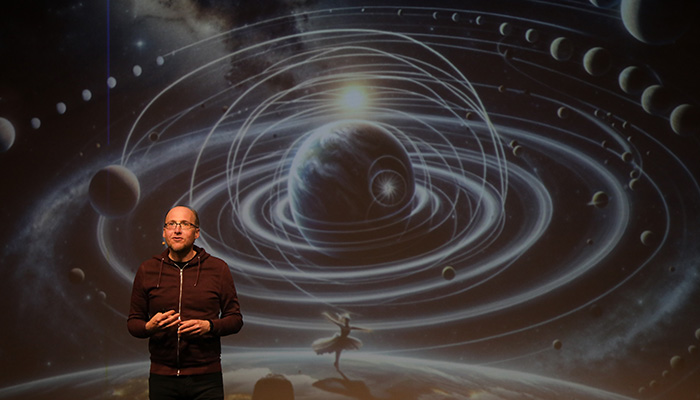 Der Astronom Florian Freistetter steht vor einer Weltraum Illustration mit Tänzerin